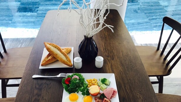 A breakfast table with a plate of eggs, bacon, ham, cheese, and vegetables, a glass of orange juice, and a croissant. - Terrace Villa Hoi An (Da Nang)