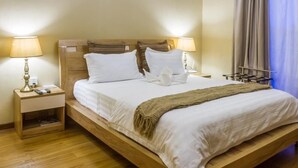 A neatly made bed with white linens and a brown throw blanket, wooden headboard, bedside tables with lamps, and a nightstand with a remote control.
