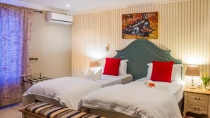 A hotel room with two beds, a bench, a wall-mounted air conditioner, and a poster.