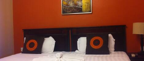 A hotel room with a large bed, two pillows with orange circles, a white blanket, and a red throw.