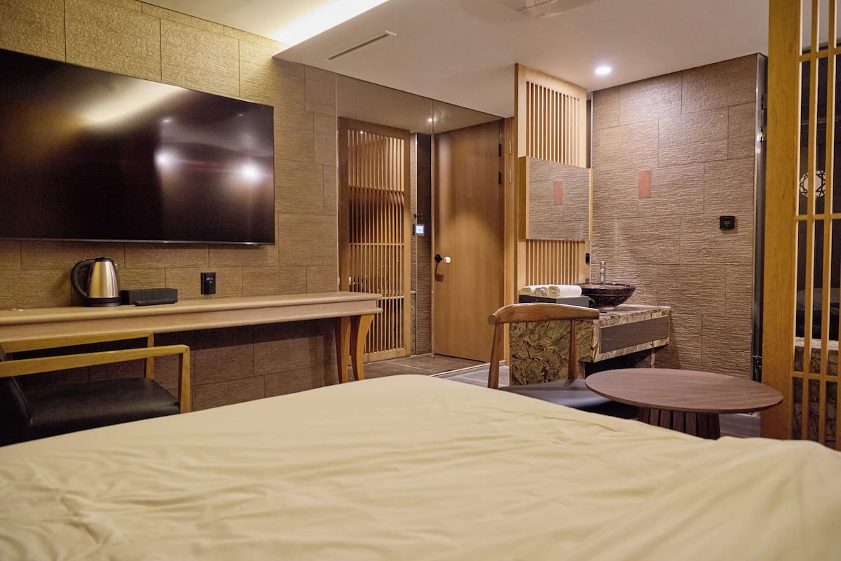 A modern hotel room with a large bed, a desk, a flat-screen TV, a sink, and a mirror.