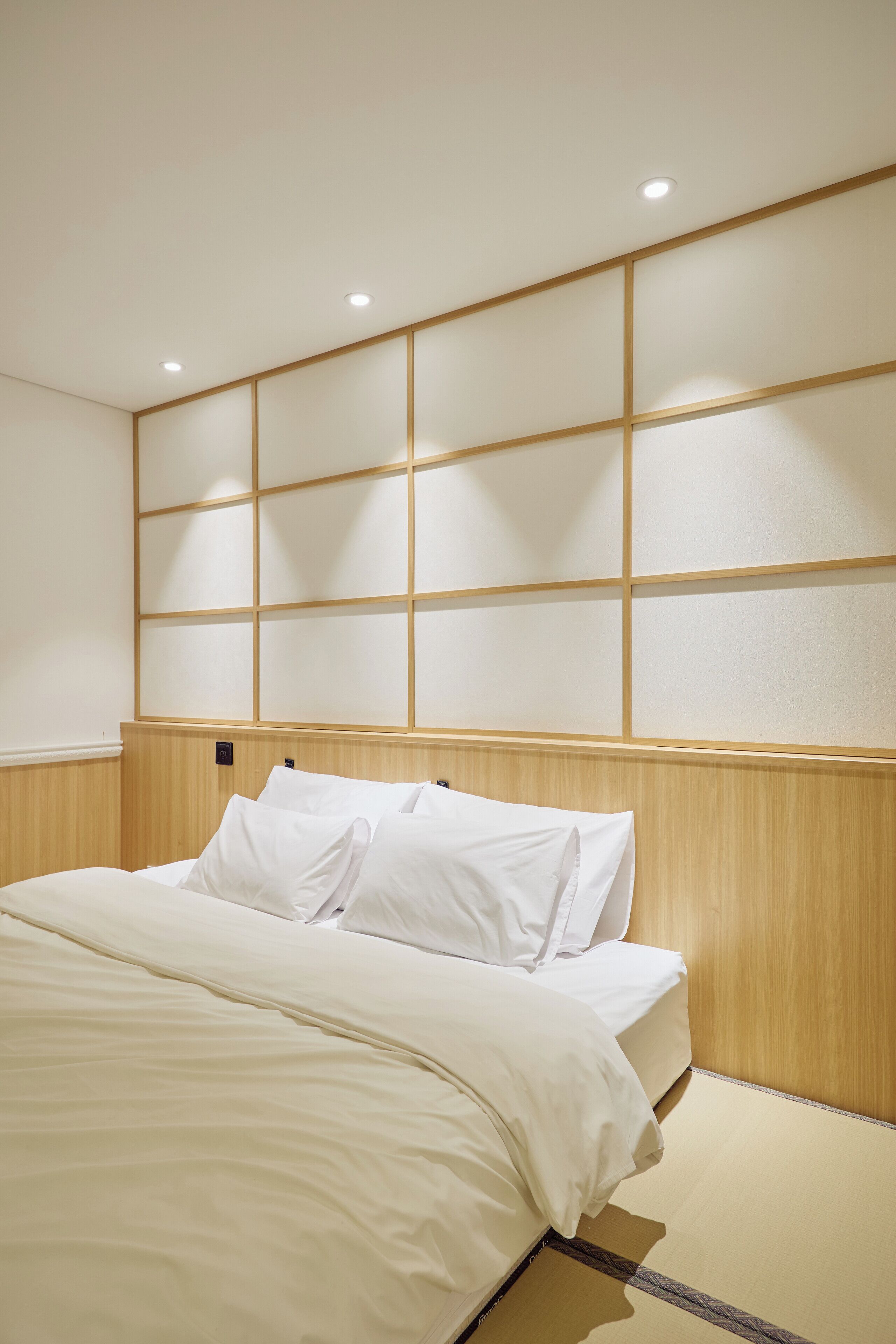 Une chambre d’hôtel avec un lit, une tête de lit en bois et des spots encastrés au plafond.