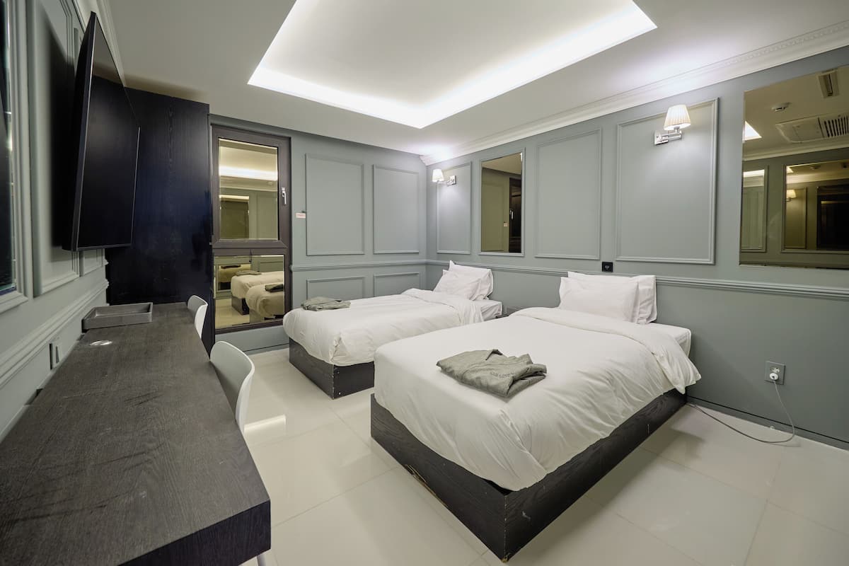 A hotel room with two beds, a desk, and a large mirror.