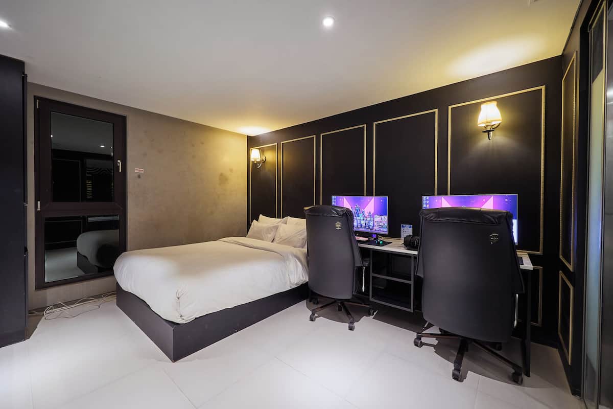 A modern hotel room with a bed, two desks, two chairs, and a large window.