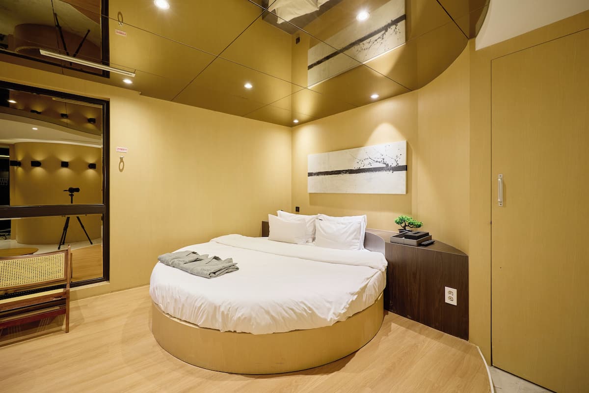 A modern bedroom with a circular bed, a wooden bench, a small desk, and a wall-mounted artwork.