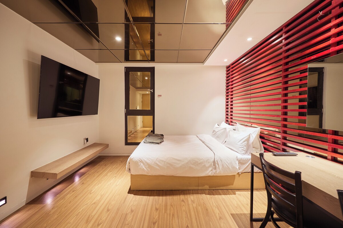 A modern bedroom with a bed, a desk, and a TV mounted on the wall.
