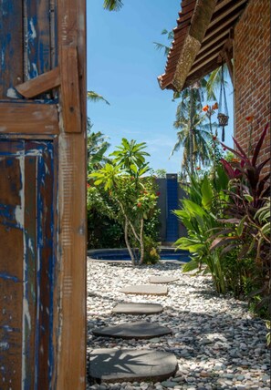 A pathway leading to a building with a rustic wooden door and a brick wall. - Villa Samalama Gili Air (Gili Air)