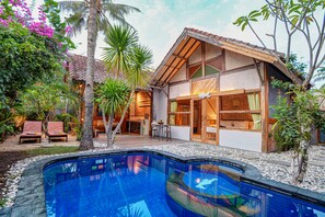 A poolside area with a house, outdoor seating, and a palm tree. - Villa Samalama Gili Air (Gili Air)