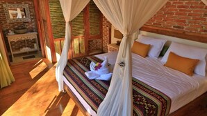 A bed with a canopy, a wooden floor, a brick wall, and a small table with a mirror. - Villas Samalama Gili Trawangan (Gili Trawangan)