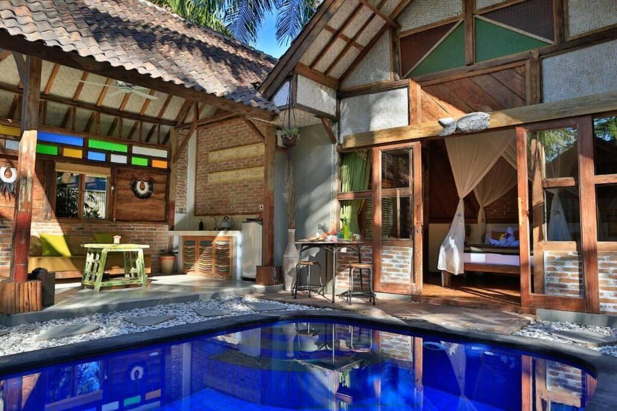 A poolside area with a brick house, wooden deck, and a clear blue pool.