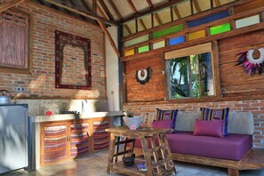 A rustic kitchen with a brick wall, wooden beams, a refrigerator, and a wooden table with a bottle and glasses. - Villas Samalama Gili Trawangan (Gili Trawangan)