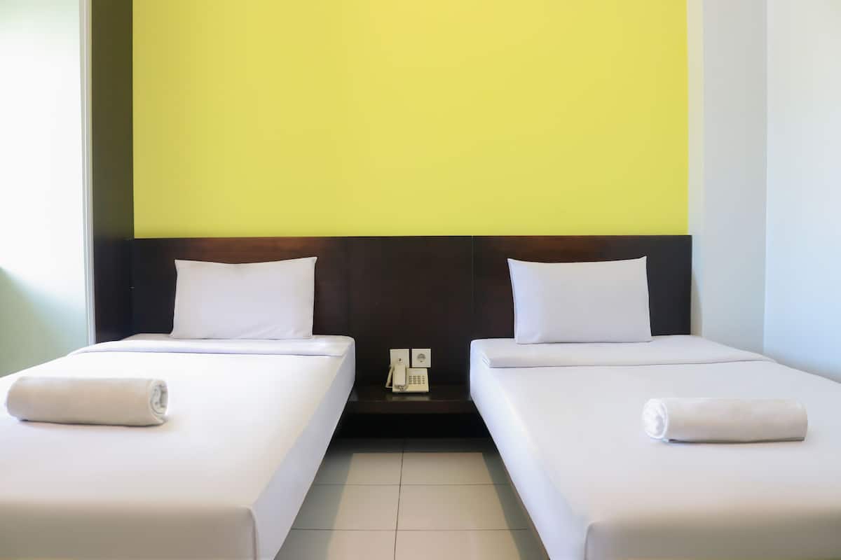 A hotel room with two single beds, a bedside telephone, and a bright yellow wall.