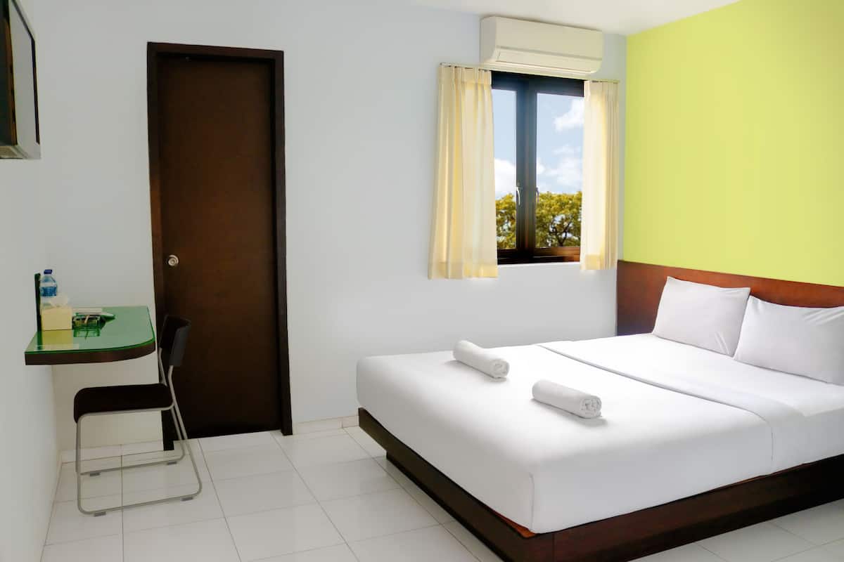 A hotel room with a bed, a desk, a chair, a window with curtains, and a door.