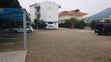 A parking area with a gravel surface, a white car, a black van, and a building with a red roof.