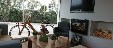 A modern living room with a large TV, comfortable seating, a wooden bicycle, and a view of the outdoors.