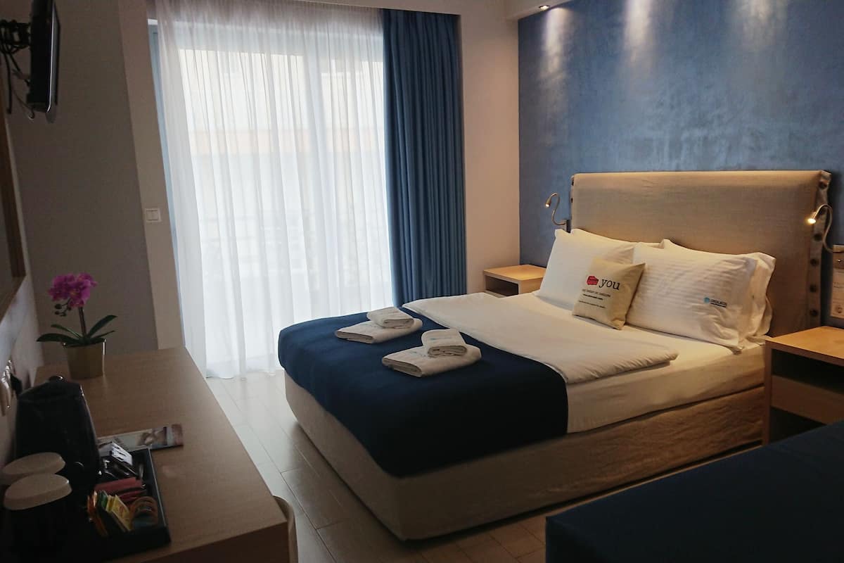Une chambre d’hôtel avec un lit, des tables de chevet, un bureau et une fenêtre avec des rideaux.