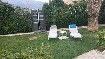 Dos sillones de exterior con una mesita y una maceta, frente a un fondo de vegetación exuberante y una vista a la montaña.