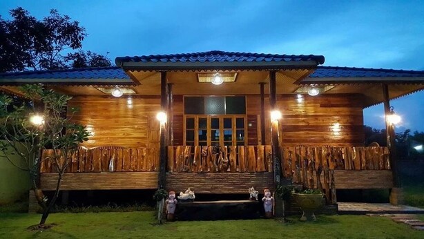 A wooden house with a tiled roof, a porch with a railing, and a window with lights. - Phupha Inn Resort (Wang Thong)
