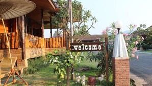 A wooden building with a 'Welcome' sign, a wooden bench, and a lamp post. - Phupha Inn Resort (Wang Thong)