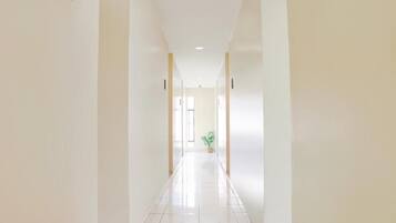 A corridor with a potted plant, white walls, and a tiled floor.