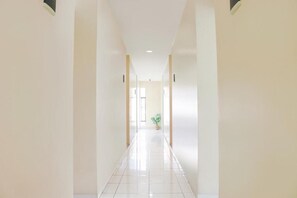 A corridor with a potted plant, white walls, and a tiled floor. - LeGreen Suite Waihaong (Ambon)