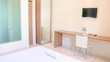 Habitación de hotel con cama, escritorio, silla, televisión y baño con puerta de vidrio.