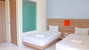 Una habitación de hotel con dos camas, un cabecero de madera, un ventanal verde y una pared blanca.