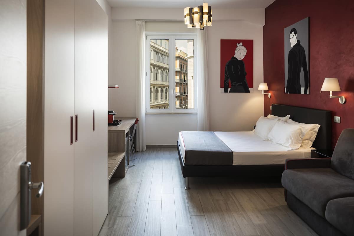 Een moderne hotelkamer met een bed, een bureau, een stoel en een raam met uitzicht op gebouwen.