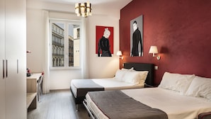 Une chambre d’hôtel avec deux lits, un bureau, une chaise, une fenêtre donnant sur des immeubles et des œuvres d’art accrochées au mur.