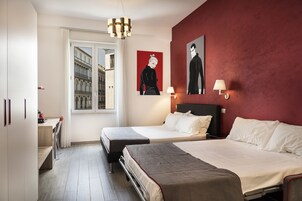 Hotellihuone, jossa on kaksi sänkyä, työpöytä, tuoli, ikkuna, josta on näkymä rakennuksiin, ja taideteoksia seinällä.