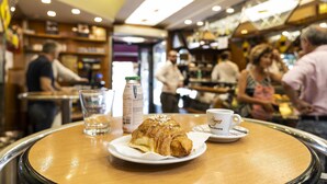 Une scène de café : une assiette avec un croissant, une tasse de café et une bouteille de lait sont posés sur la table.