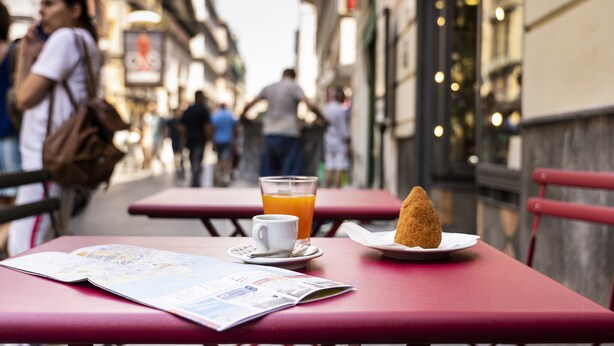 Une table avec un menu, un verre de jus d’orange et un croissant.