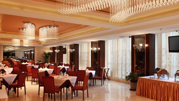 Un comedor amplio con varias mesas y sillas, elegantes candelabros y ventanas grandes con cortinas.