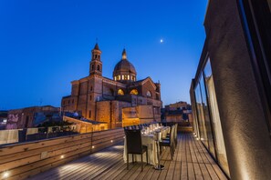 A rooftop terrace with a view of a historic building, including a bell tower and dome, and a wooden deck with tables and chairs. - Alba Palace Hotel (Favara)