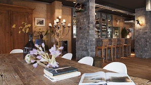 A wooden dining table with books and a vase of flowers, a bar area with stools, and a stone pillar.