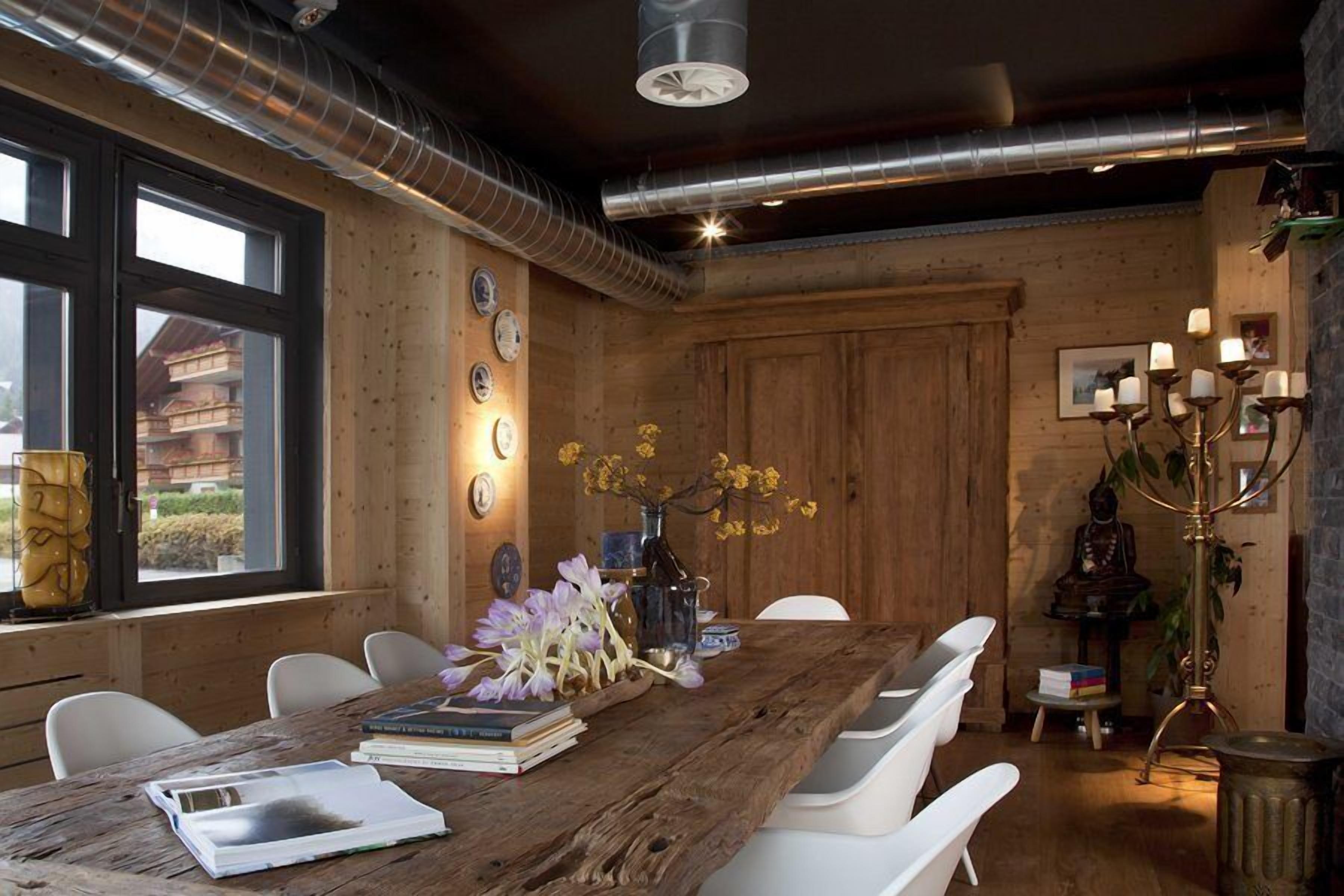 A rustic wooden dining room with a large table, white chairs, and a chandelier.