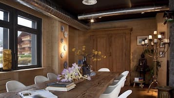 A rustic wooden dining room with a large table, white chairs, and a chandelier.