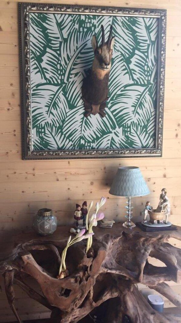 A wooden wall with a framed picture of a rabbit, a rustic wooden table with a vase of flowers, and a lamp. - Boutique-Hôtel Chez Jan (Troistorrents)