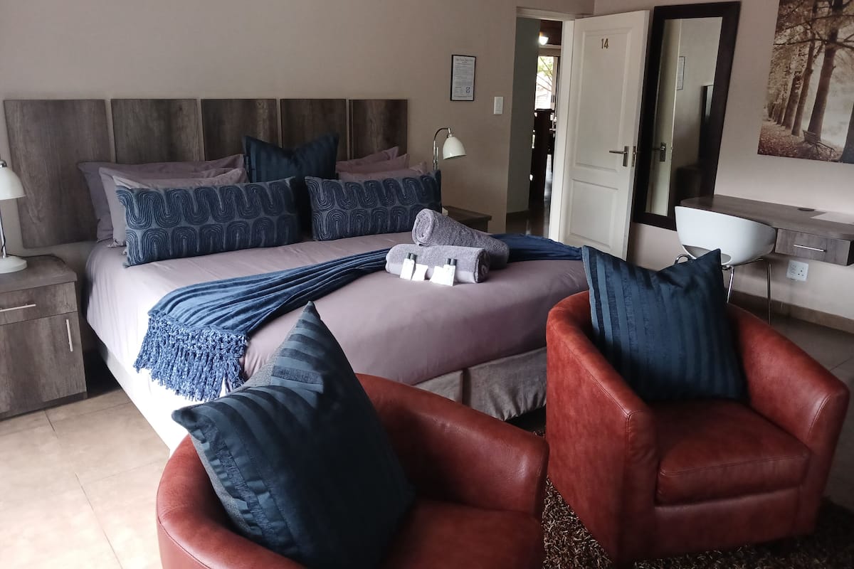 A bedroom with a bed, pillows, a chair, a desk, and a mirror.