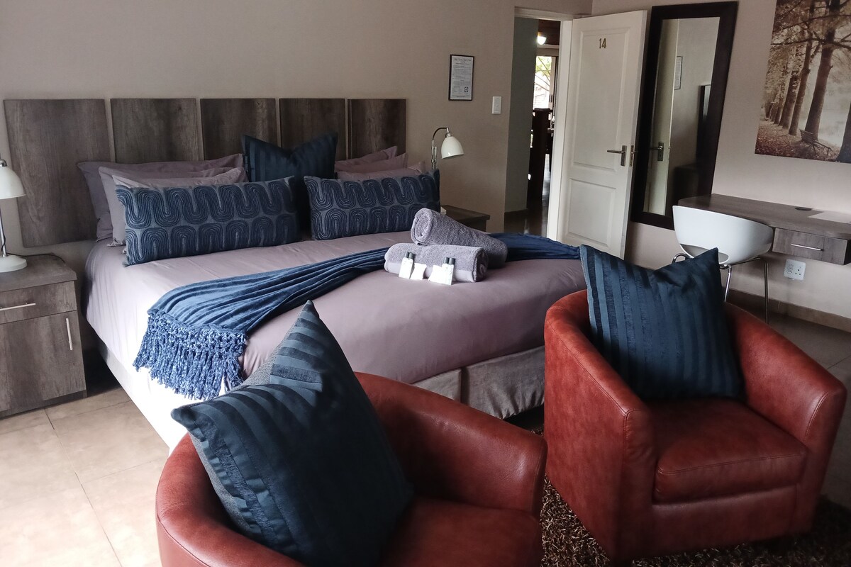 Ein Schlafzimmer mit einem Bett, Kissen, einem Sessel, einem Schreibtisch und einem Spiegel.