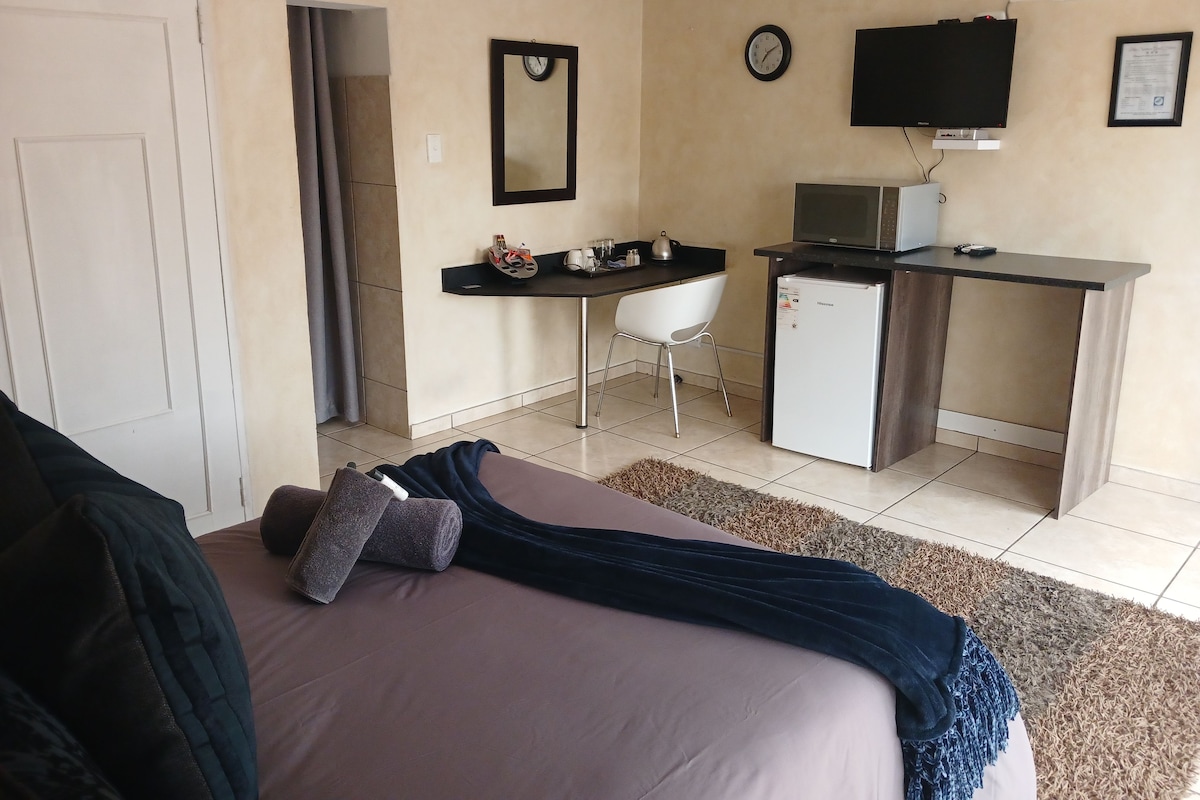 Una habitación de hotel con cama, escritorio, televisión, refrigerador y un reloj en la pared.