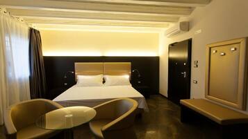 Una habitación de hotel con una cama, dos sillas, una mesita, un banco y un espejo.