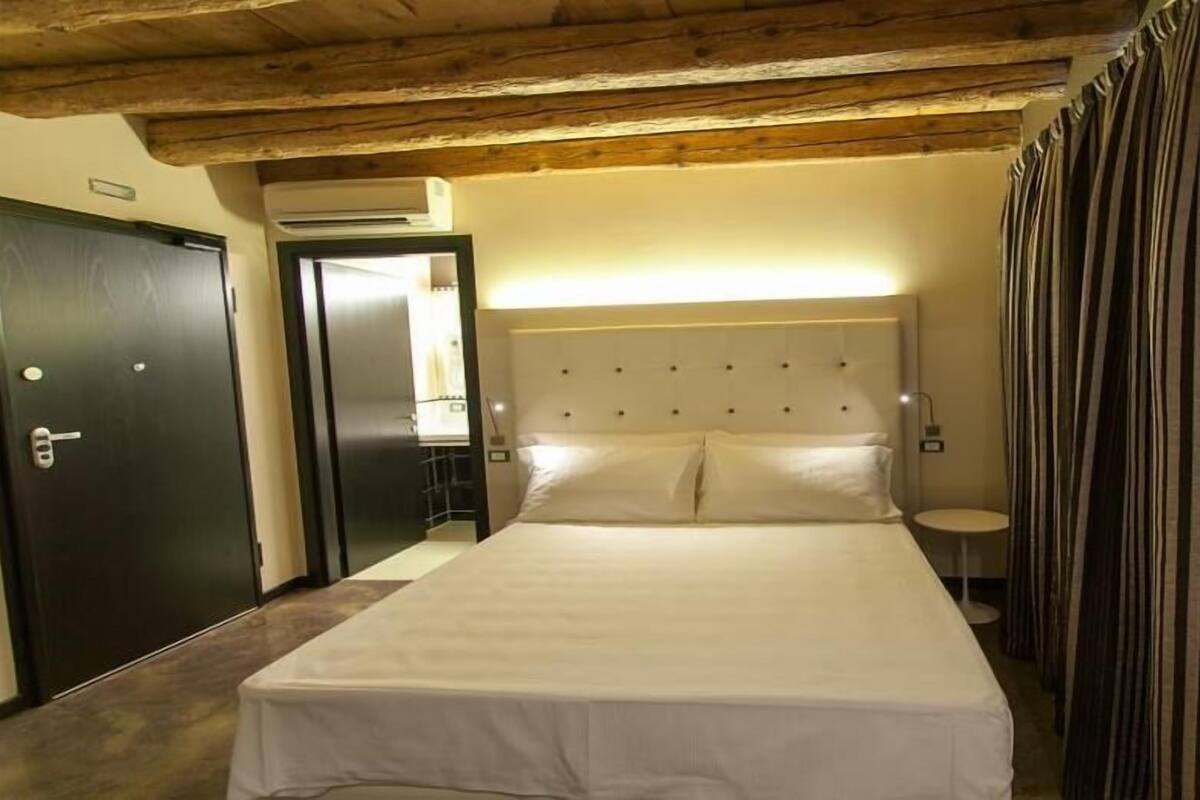A hotel room with a large bed, a wooden ceiling, a wall-mounted TV, and a door with a key lock.
