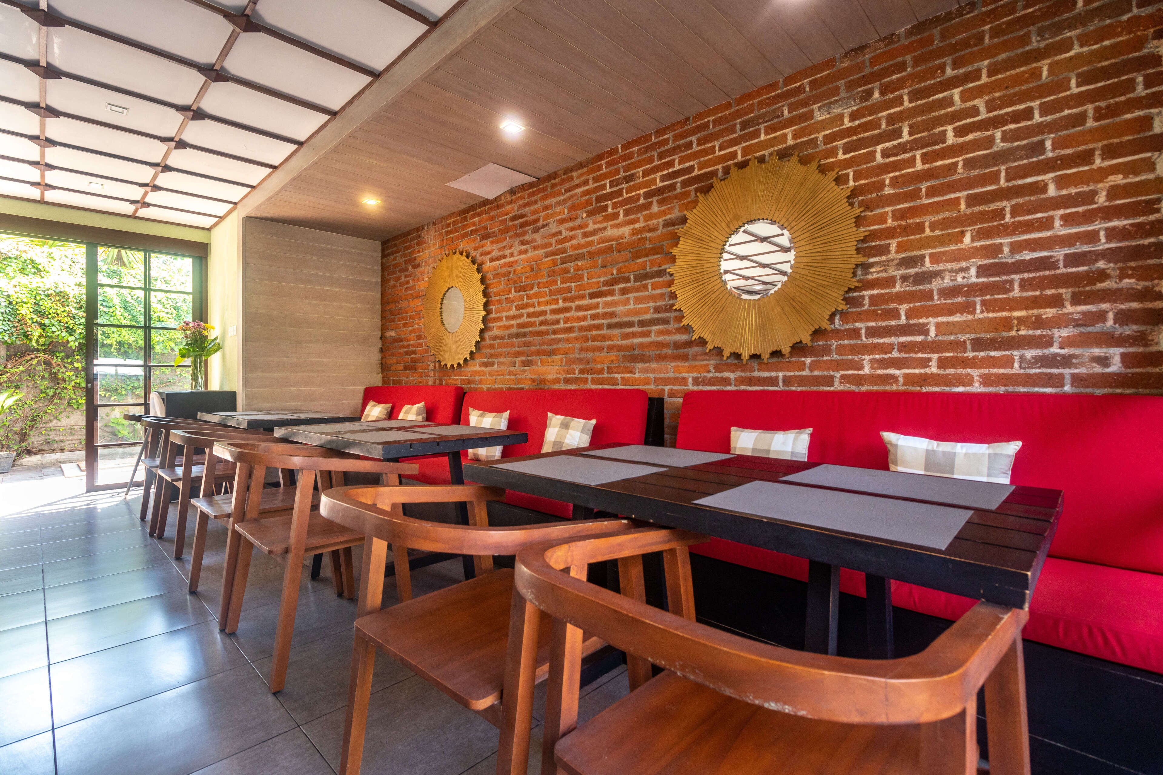 A restaurant with brick walls, wooden tables, and red seating.