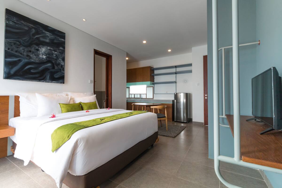 Una habitación de hotel moderna con una cama grande, un escritorio, una kitchenette y un televisor.