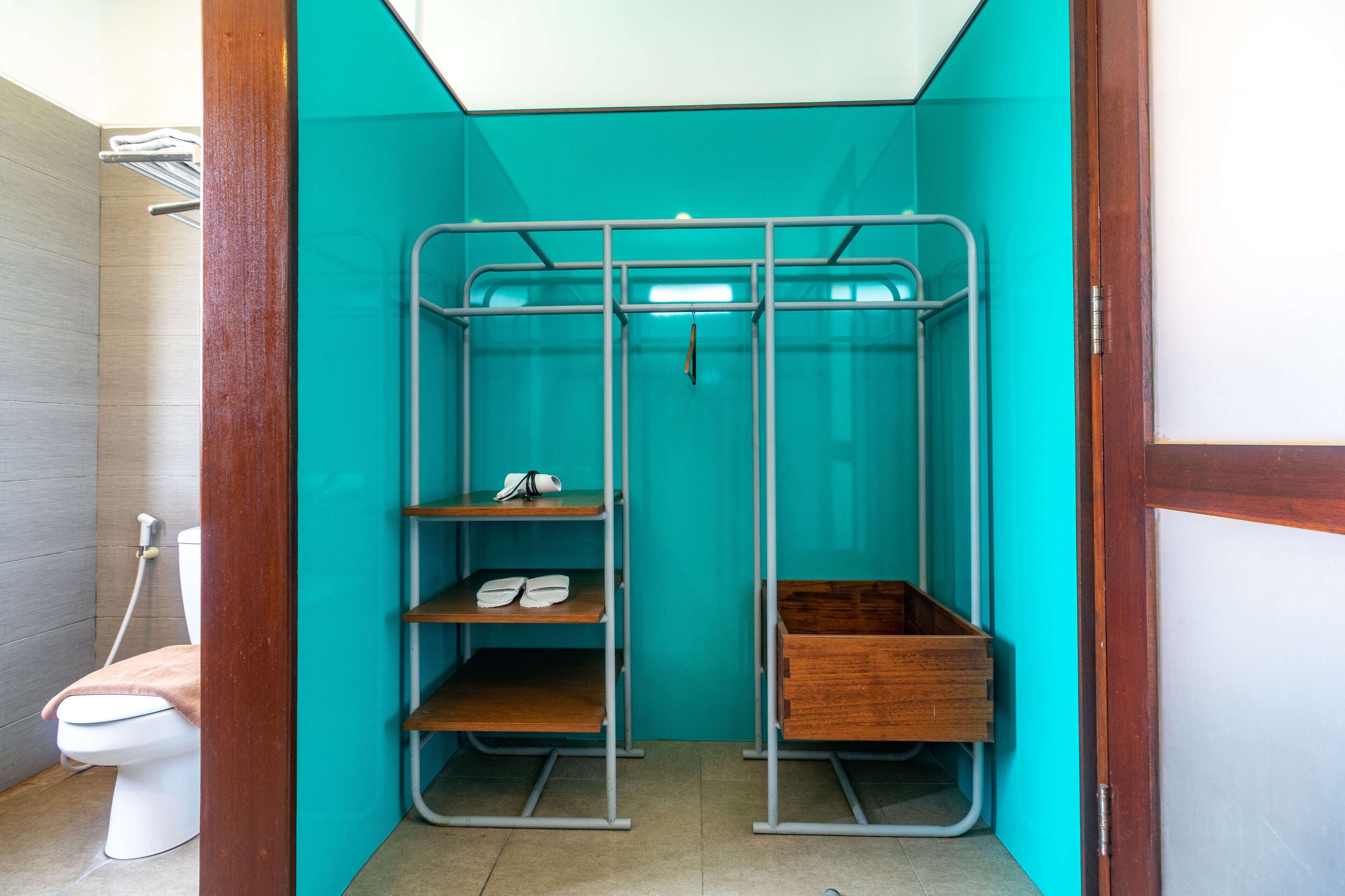 A compact bathroom with a toilet, a shower stall, and a wooden shelf unit with a hanging towel rack.