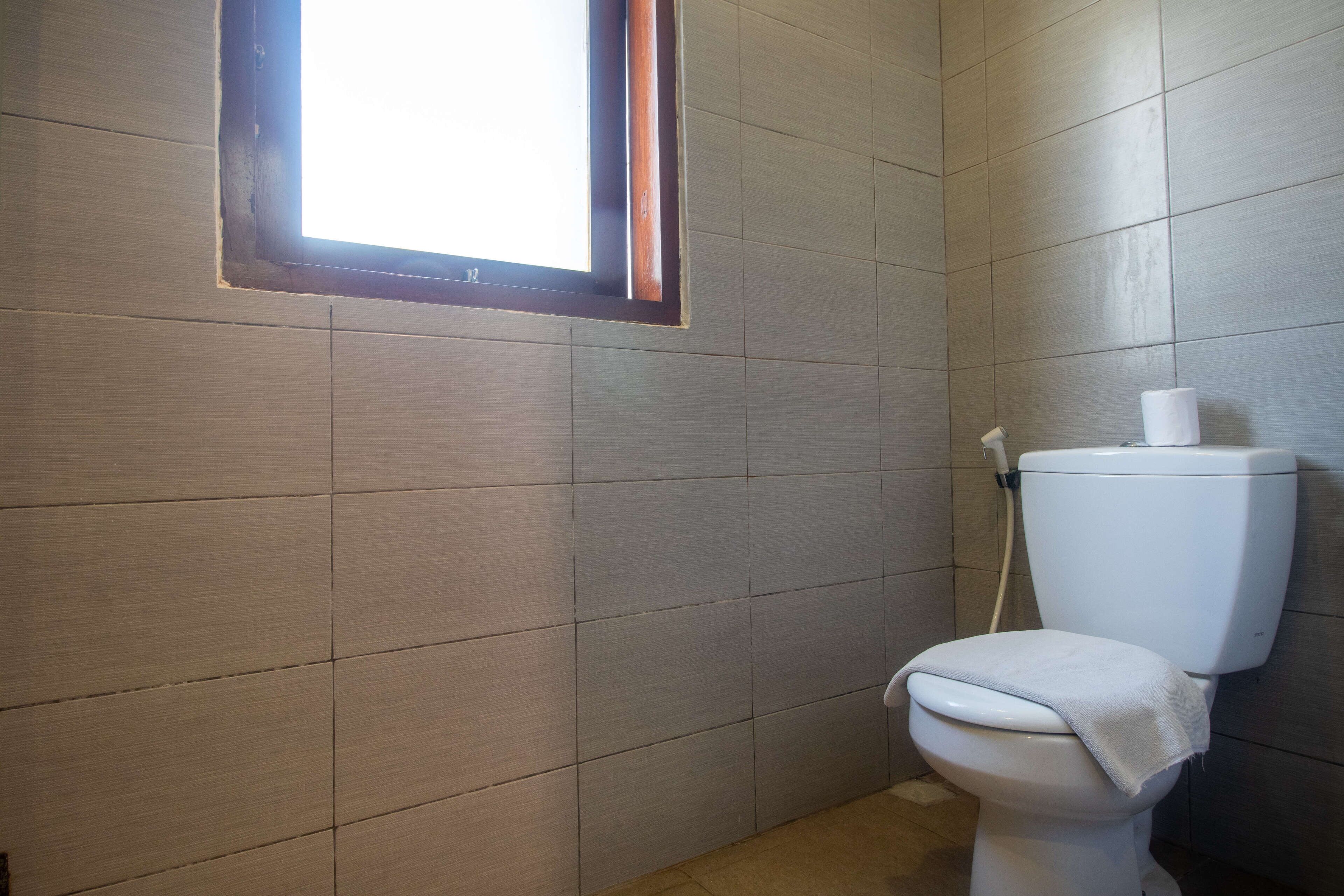 A bathroom with a toilet, a window, and tiled walls.