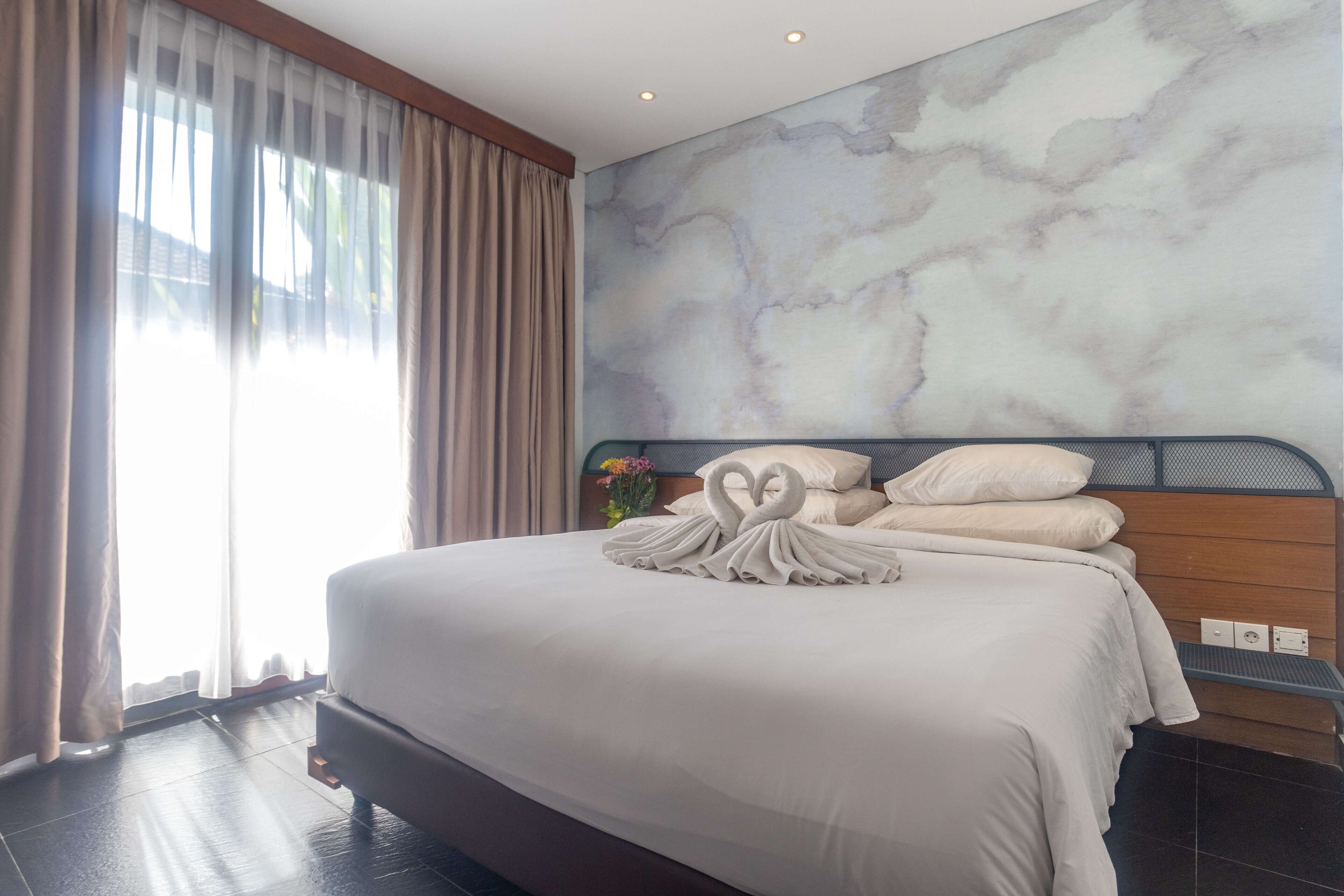 A hotel room with a large bed, a marble wall, and a window with curtains.