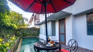 Zona junto a la piscina con una mesa, sillas y una sombrilla.