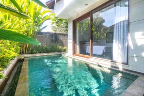 Una piscina con cerramiento de vidrio, rodeada de exuberante vegetación y un edificio moderno con grandes puertas correderas de vidrio.